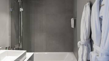 Een moderne badkamer met een douchecabine van glas, een wit bad en twee witte badjassen aan haken.