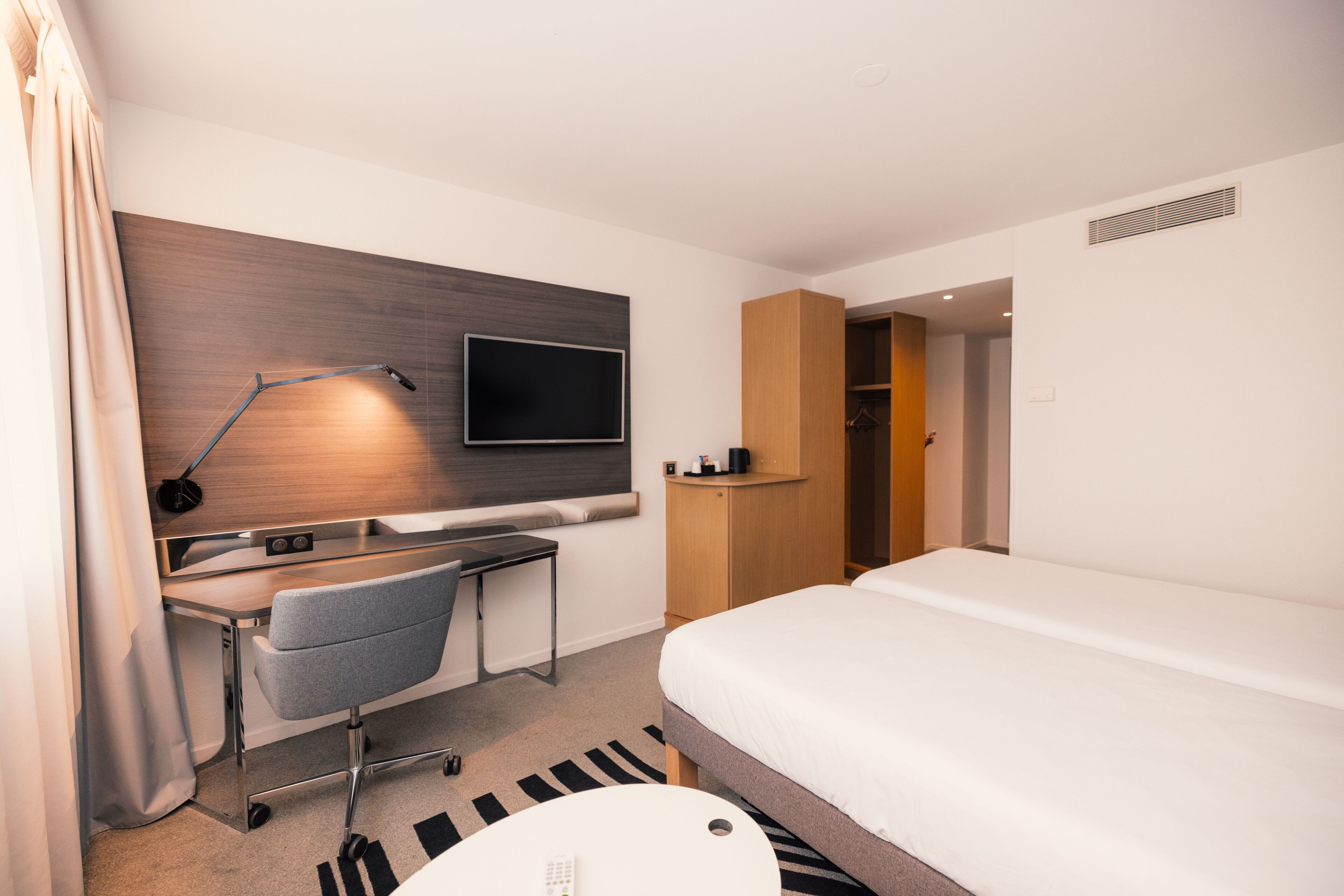 Habitación de hotel con cama, escritorio, silla, televisor y armario.
