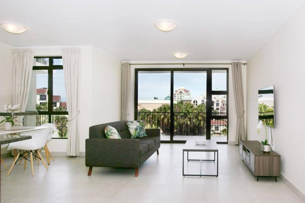 Een moderne woonkamer met een bank, een eettafel en stoelen, een televisie en een balkon met uitzicht op de stad.