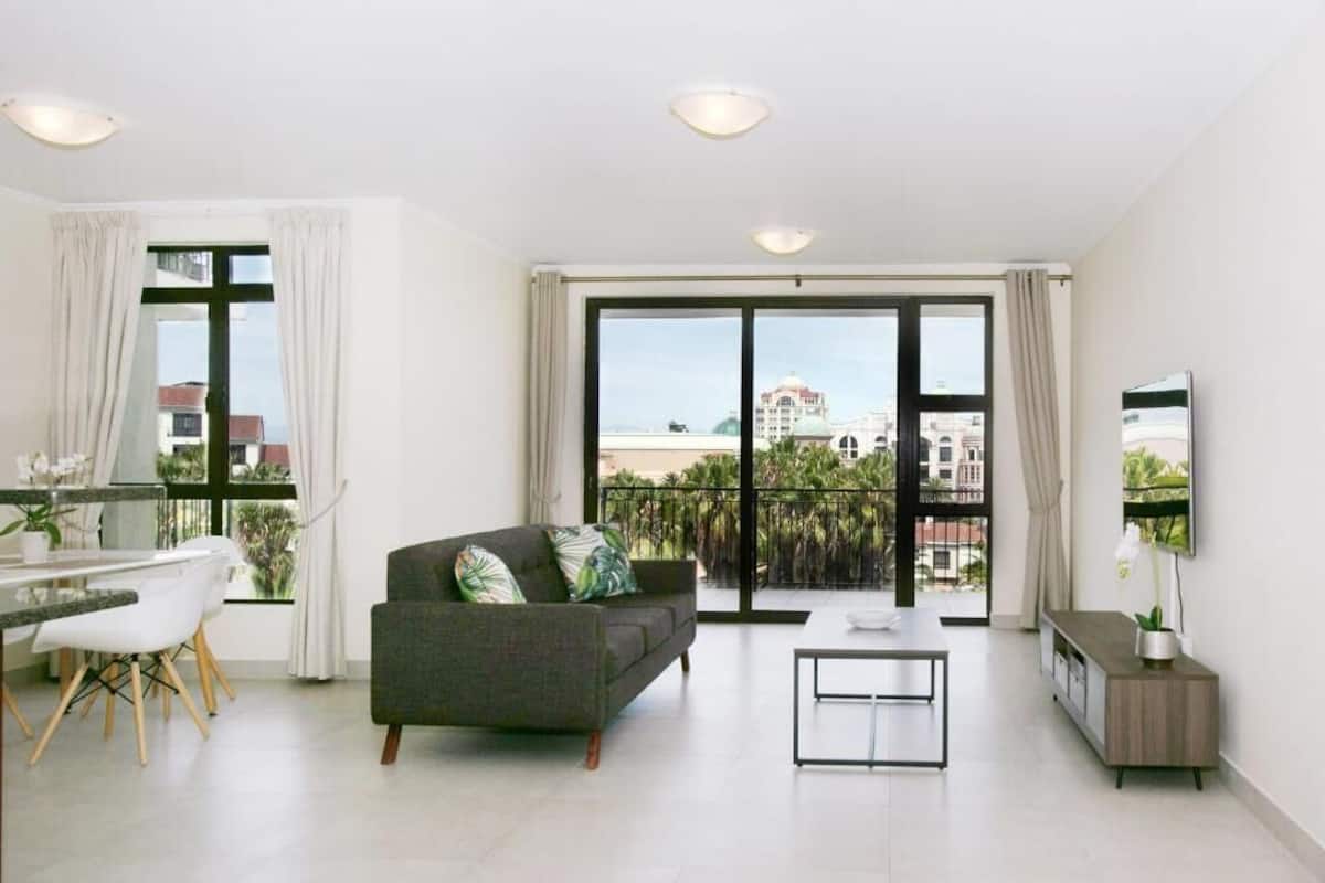 Een moderne woonkamer met een bank, een eettafel en stoelen, een televisie en een balkon met uitzicht op de stad.