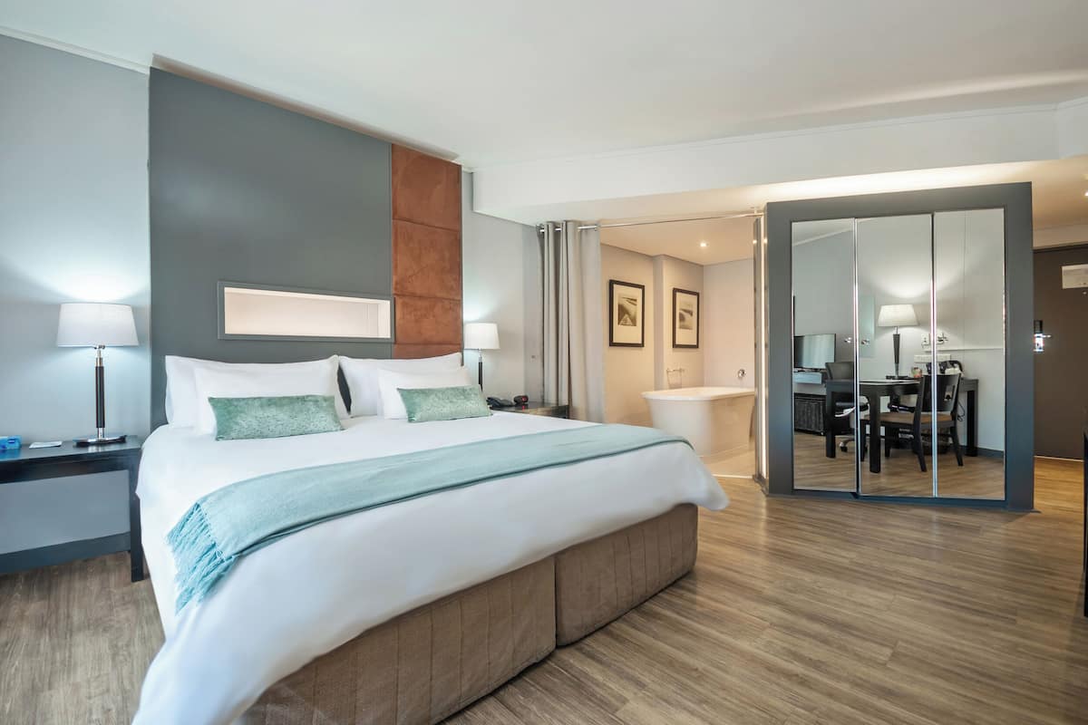 Een moderne hotelkamer met een groot bed, nachtkastjes, een badkamer met douche en een zithoek met een tafel en stoelen.