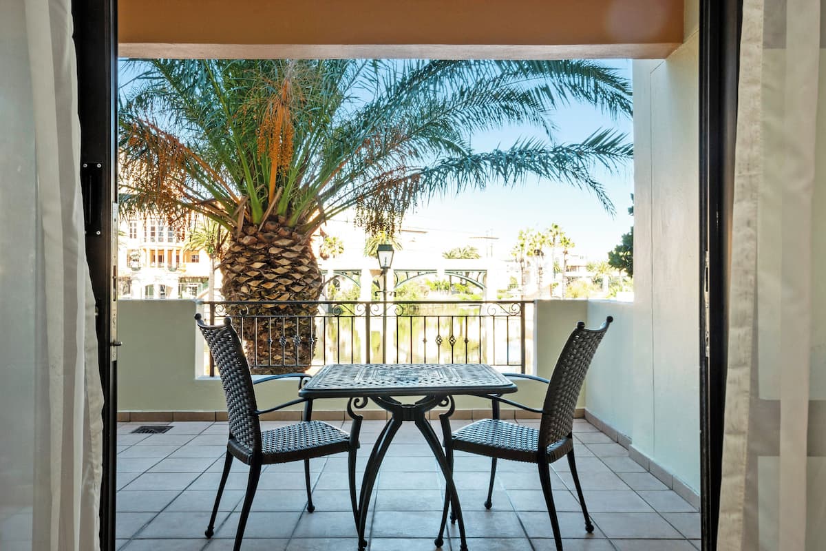 Een balkon met een tafel en stoelen, een palmboom en uitzicht op gebouwen.