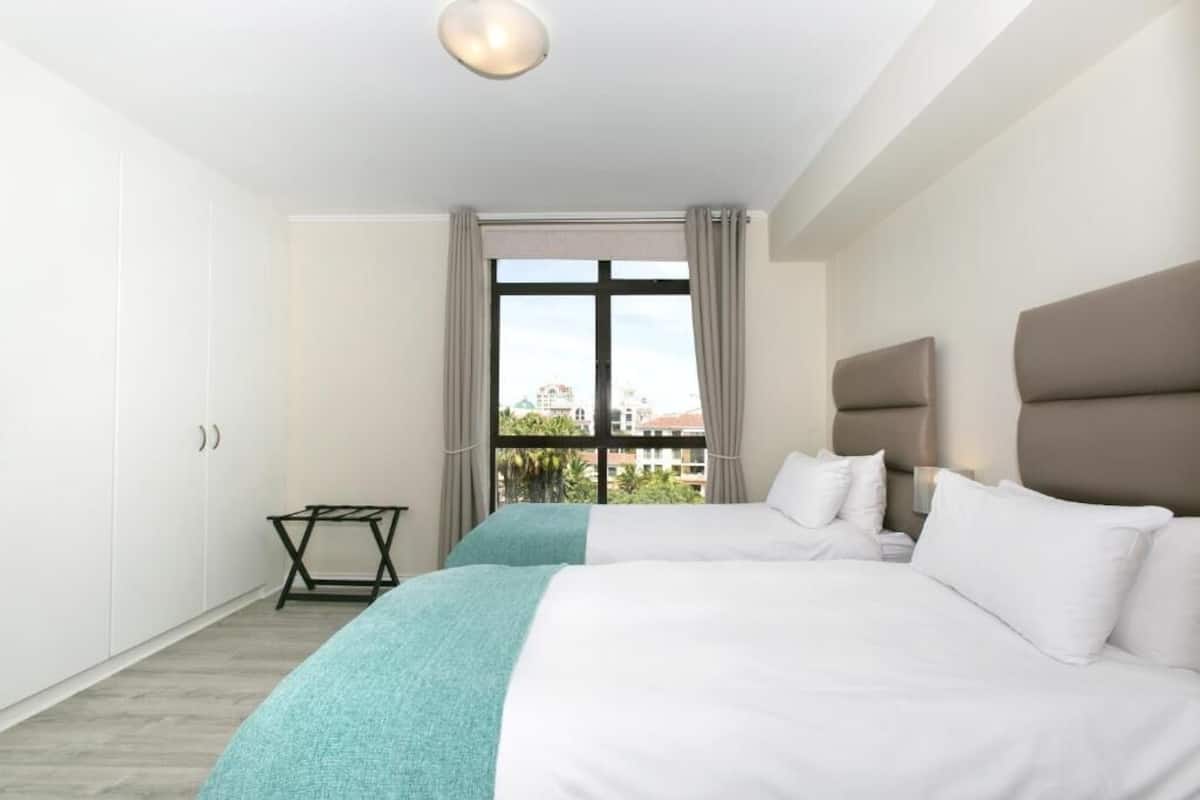Hotelkamer met twee bedden, een raam met gordijnen, een tafeltje en uitzicht op gebouwen.