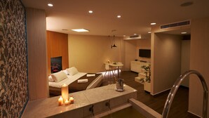 Een moderne hotelkamer met een wellnessruimte, inclusief een badkuip, een zithoek met een bank en een klein tafeltje, en een aan de muur bevestigde televisie.