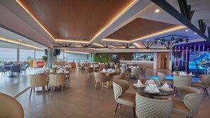 Een ruim restaurant met hoge plafonds, modern licht en verschillende zithoeken.