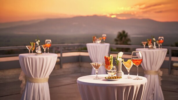 Een terras met ronde tafels klaar voor een diner, met uitzicht op een prachtig zonsondergang.