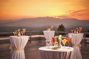 A terrace with round tables set for dining, overlooking a scenic sunset view.