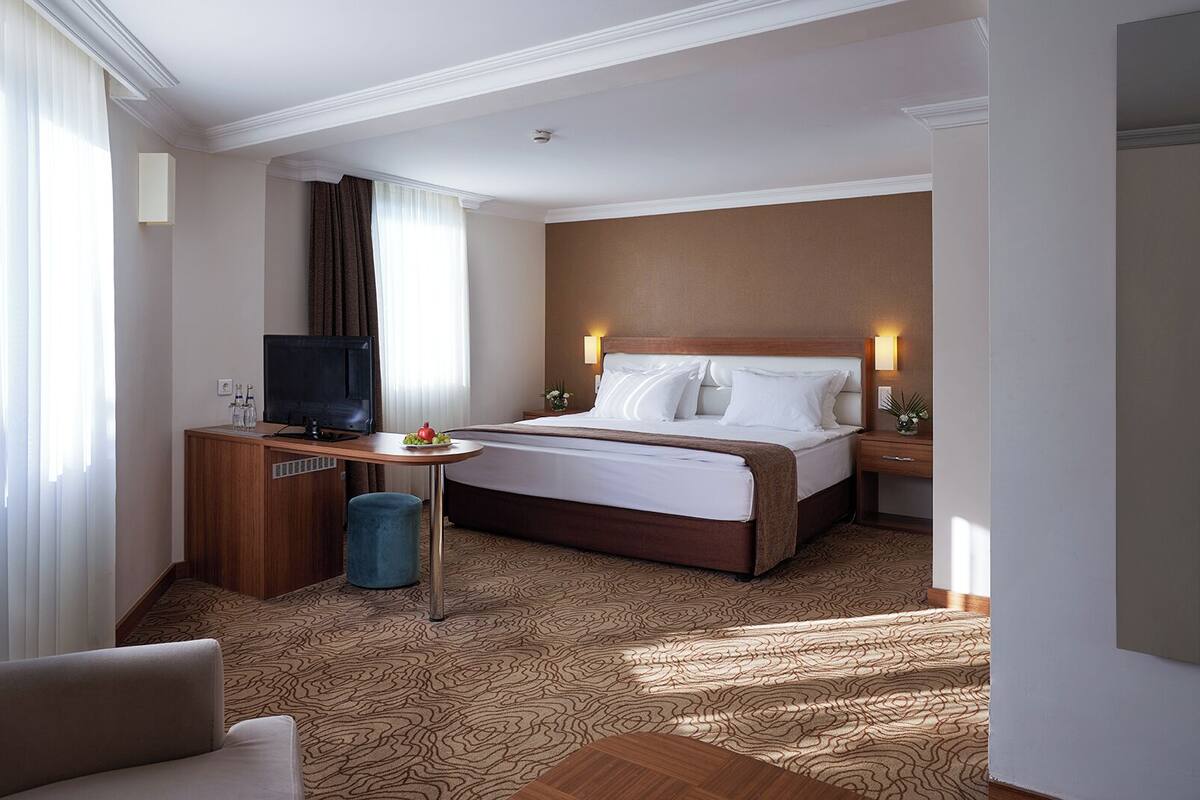 Een hotelkamer met een bed, een bureau met een televisie, een stoel en een klein tafeltje met een schaal fruit.