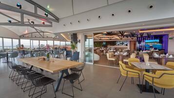 Un comedor amplio con varias mesas y sillas, una zona de bar con una pantalla grande, y vistas al exterior.