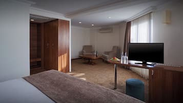 A hotel room with a bed, a desk with a TV, a chair, a small table with a bottle and glasses, and a wardrobe.