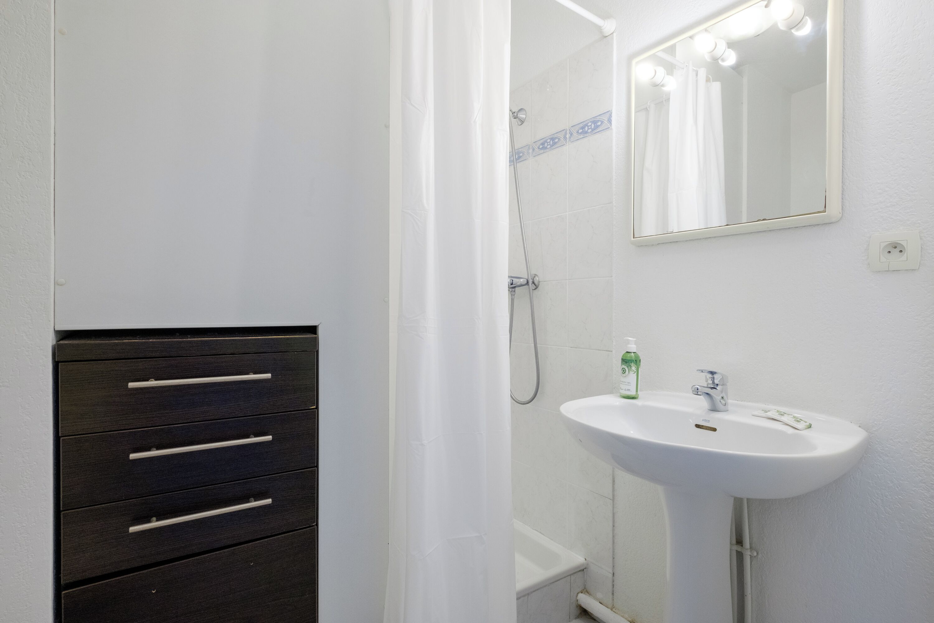 A bathroom with a white sink, a mirror, and a dark wooden cabinet with drawers.