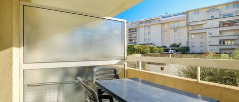 A balcony with a table and chairs, a large window, and a view of residential buildings.
