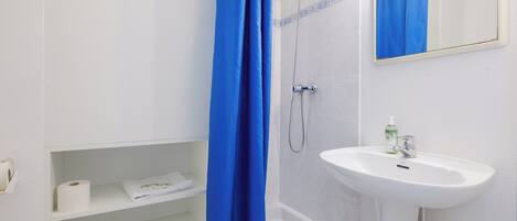 Un baño con un lavamanos blanco, una ducha con cortina azul y un espejo sobre el lavamanos.