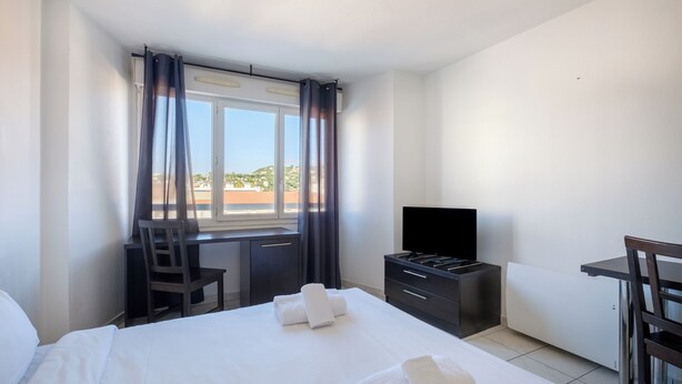A hotel room with a bed, a desk, a chair, a TV, and a window with curtains.