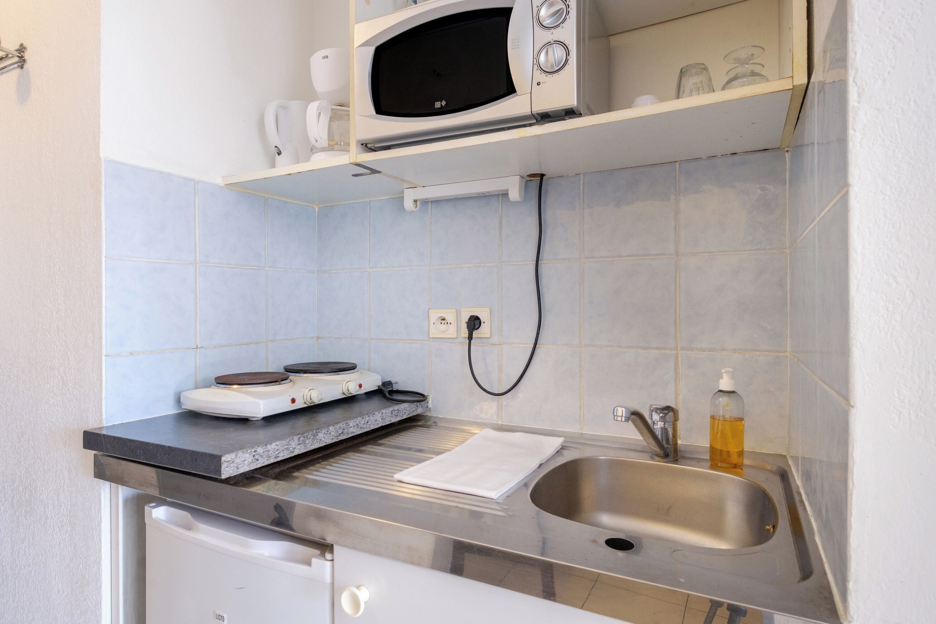 Una cocina compacta con microondas, hervidor y tetera sobre la encimera.