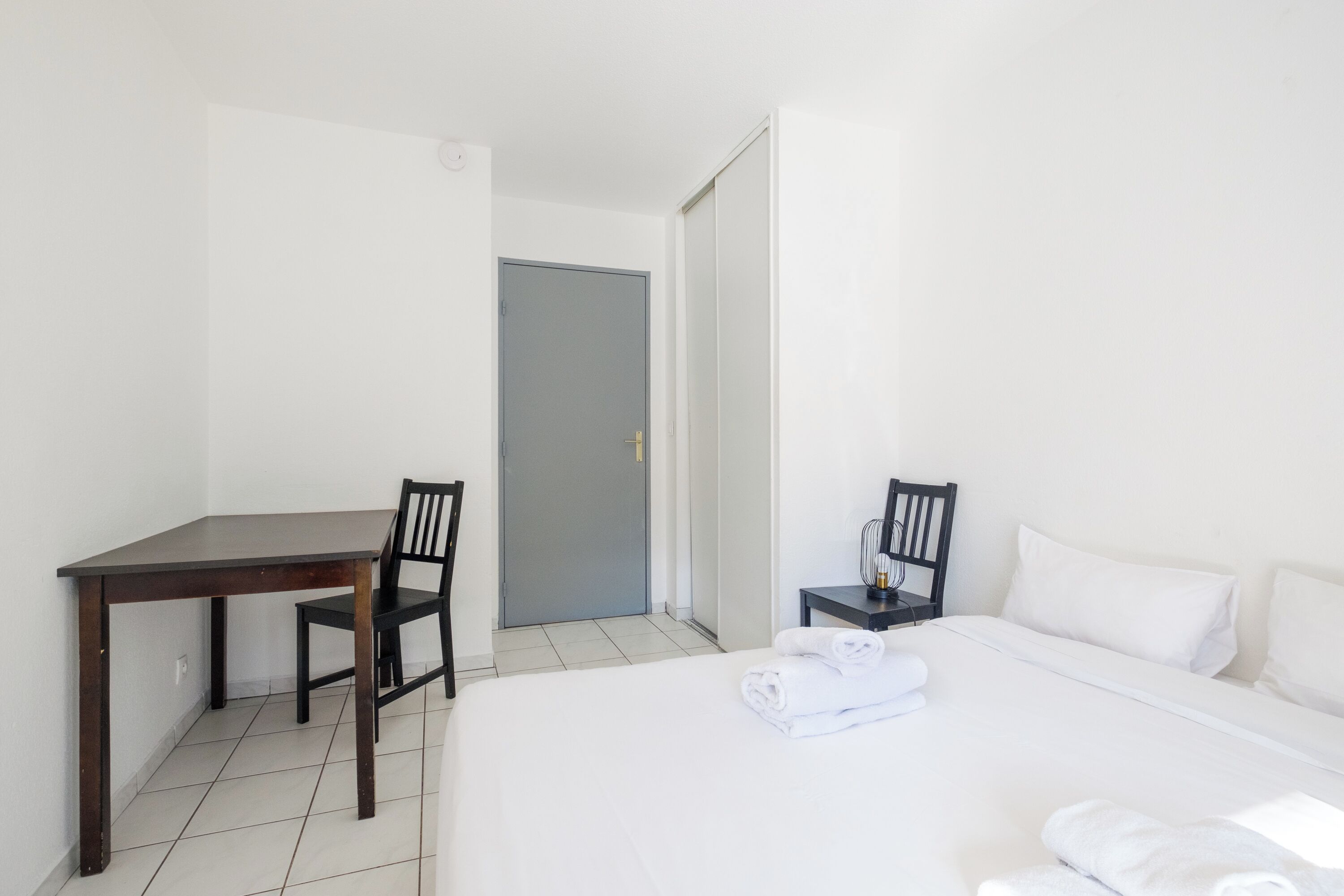 Een hotelkamer met een bed, een bureau, twee stoelen en een deur.