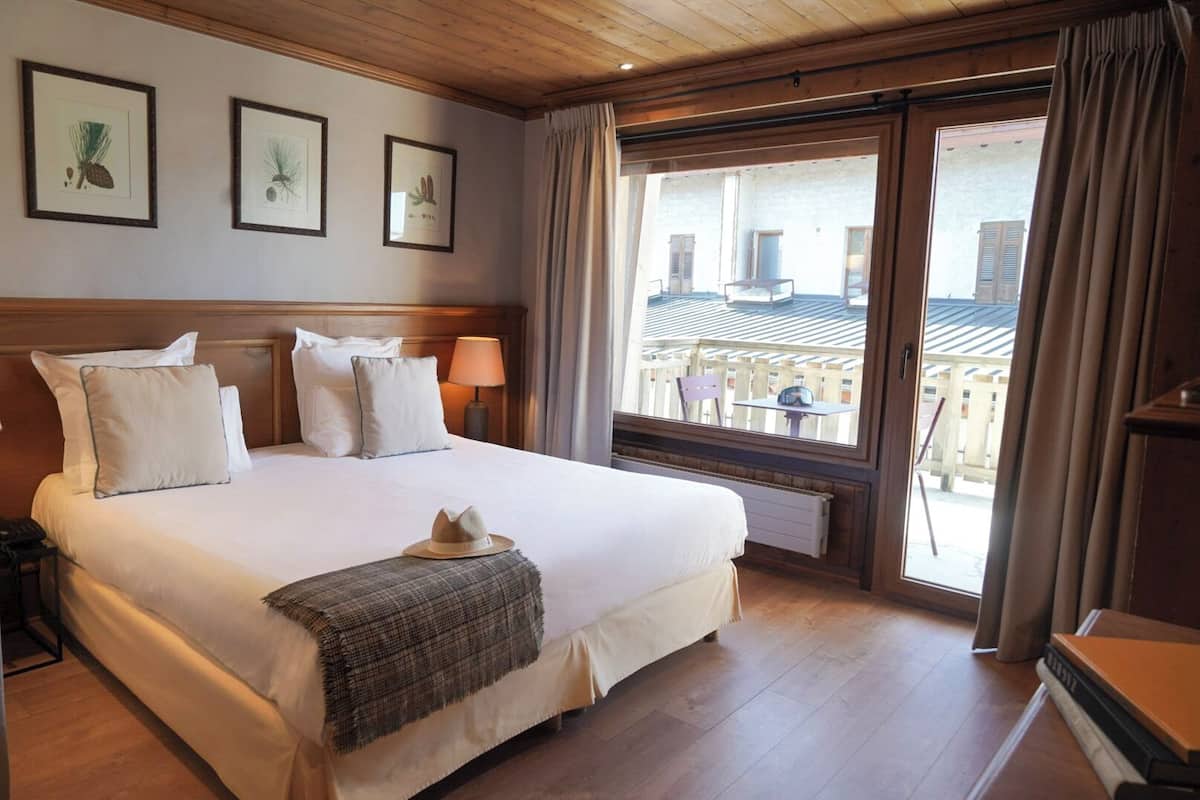 Habitación de hotel con una cama grande, una mesita de noche, una lámpara y una ventana con vistas al exterior.