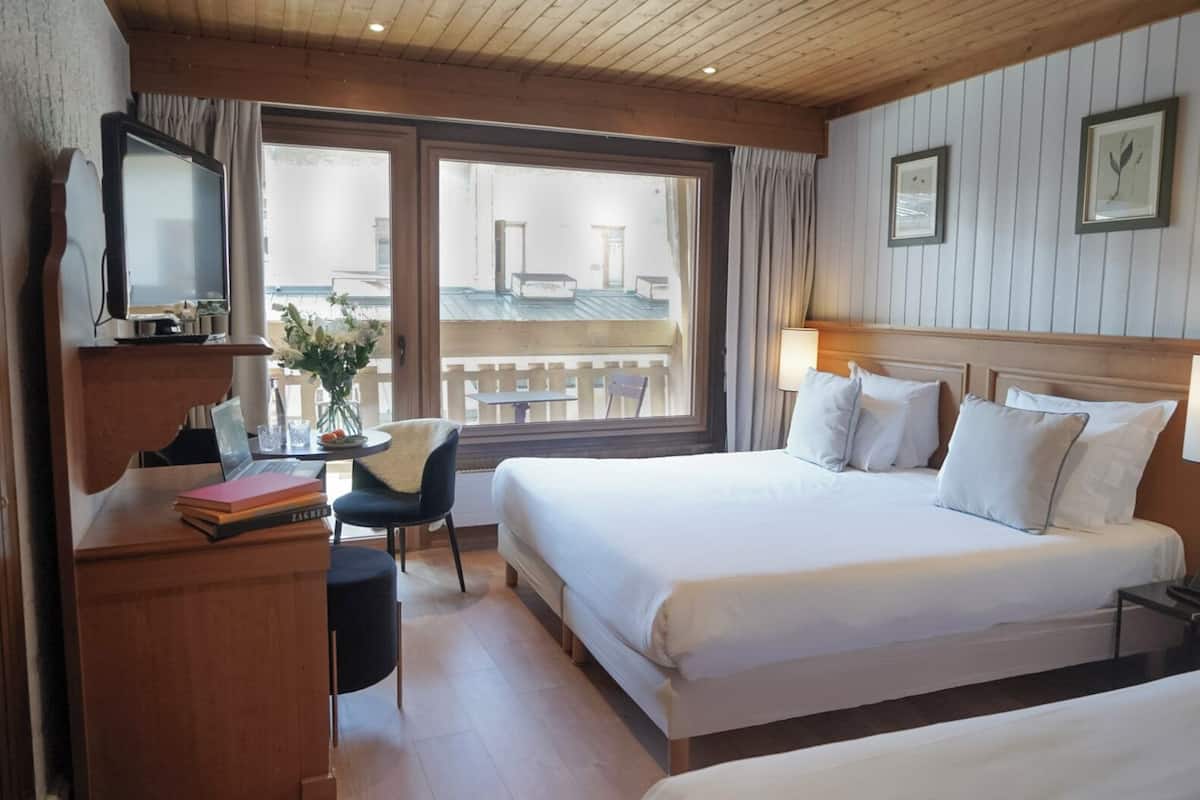 Habitación de hotel con una cama grande, un escritorio con computadora, una silla y ventana con vistas al exterior.
