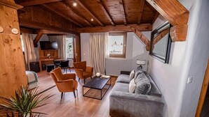 Ein gemütliches Wohnzimmer mit Holzbalken, einem grauen Sofa, orangefarbenen Sesseln und einem schwarzen Couchtisch.