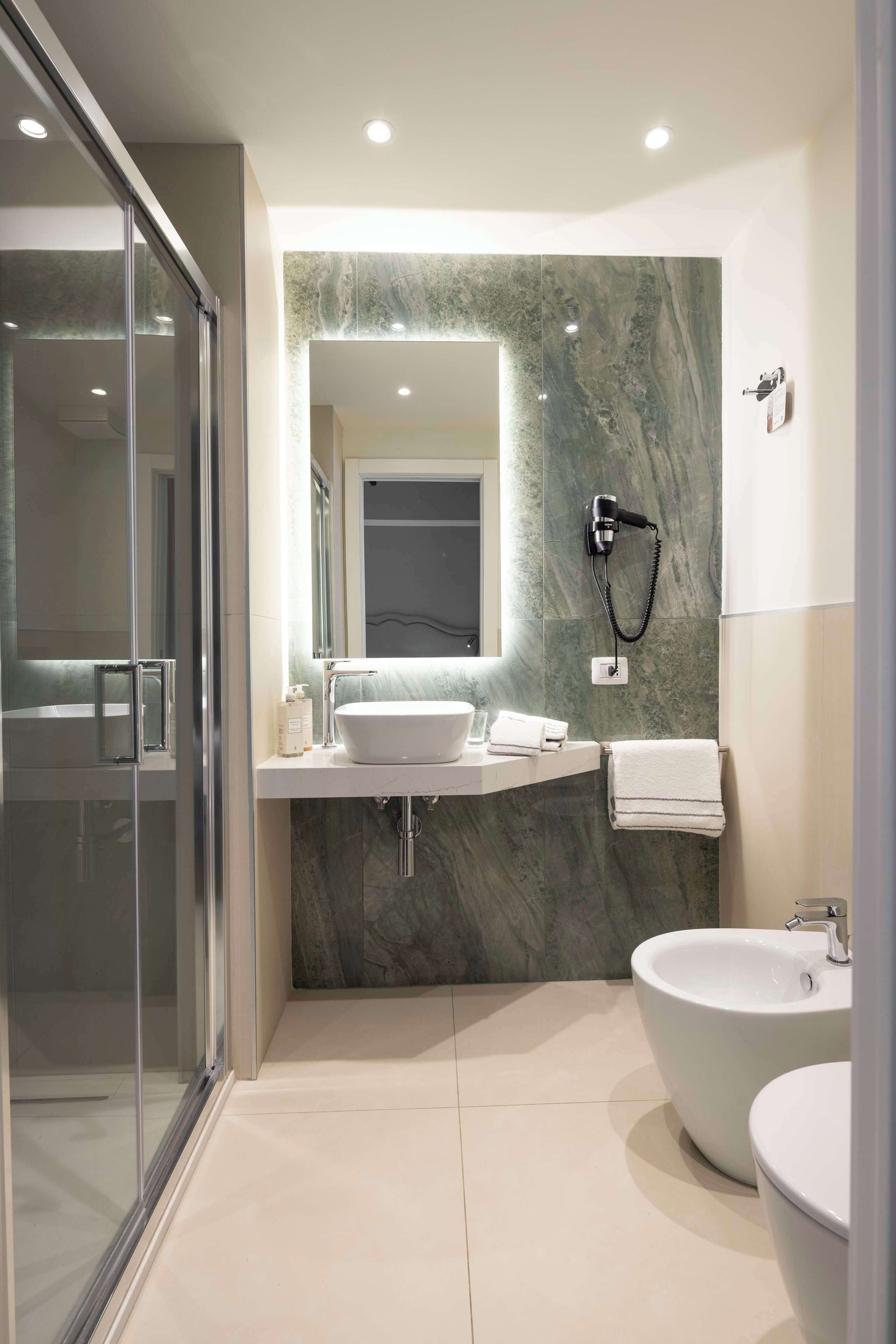 Une salle de bain moderne avec une douche à l’italienne en verre, un pare-baignoire en marbre et une grande baignoire sur pied.