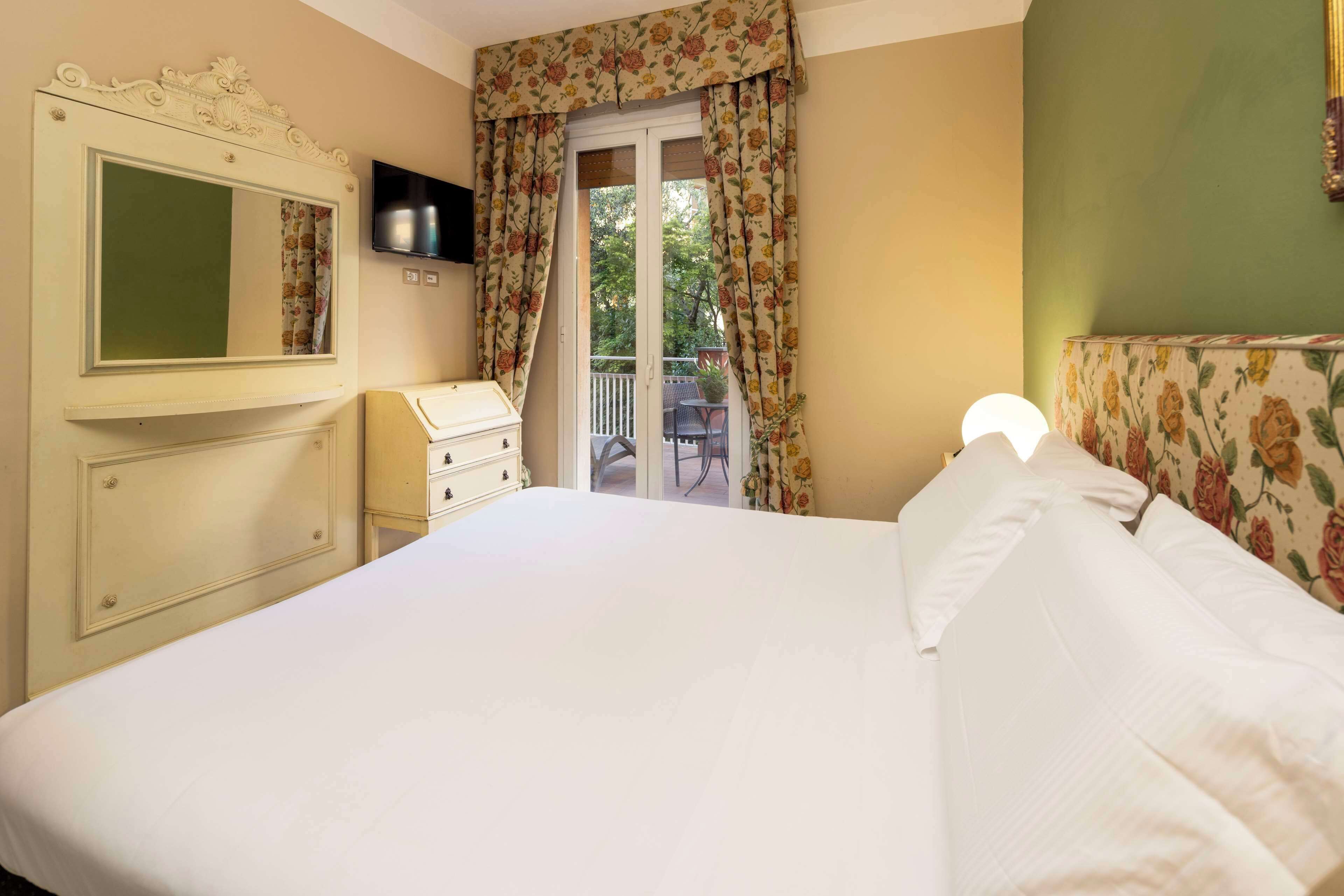 A bedroom with a bed, a dresser, a television, and a balcony with a chair.