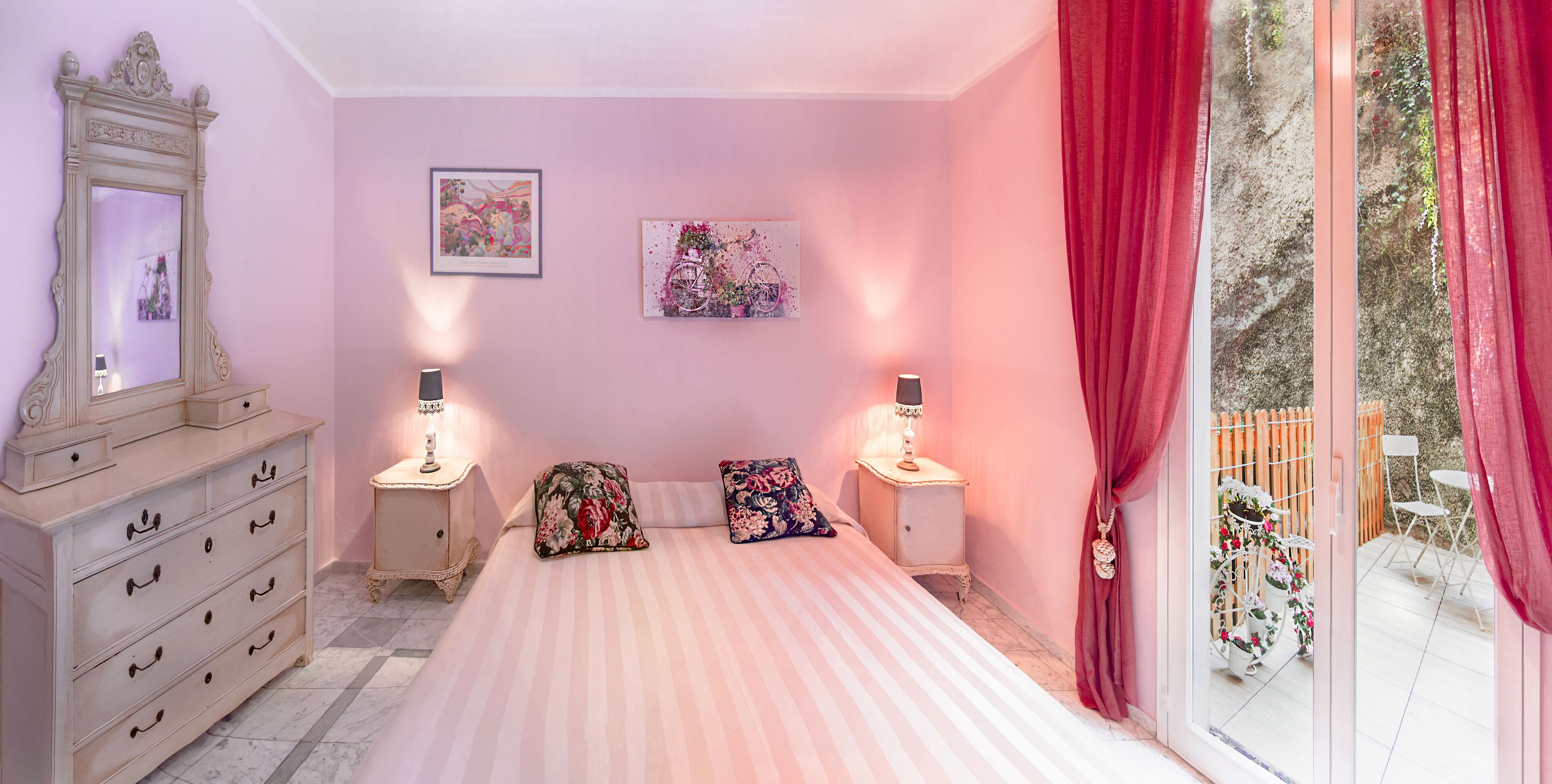 Een slaapkamer met een bed, een dressoir, twee nachtkastjes met lampen en een raam met gordijnen.