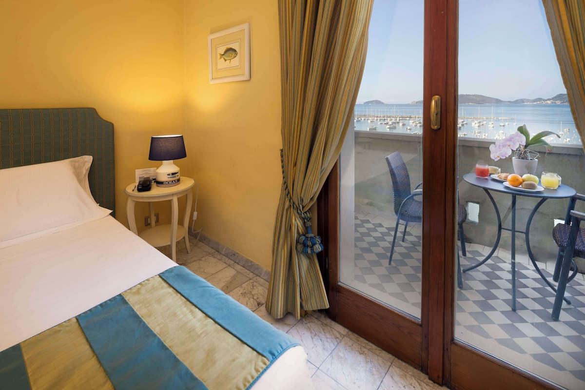 Una camera d'albergo con un letto, un tavolino con una lampada, un quadro appeso e un balcone con apparecchiatura per la colazione.
