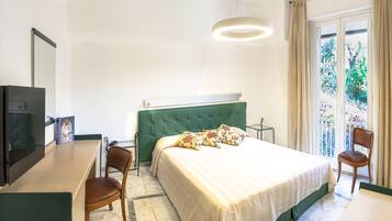 Habitación de hotel con cama, escritorio, silla, televisor y vista a zonas verdes por la ventana.