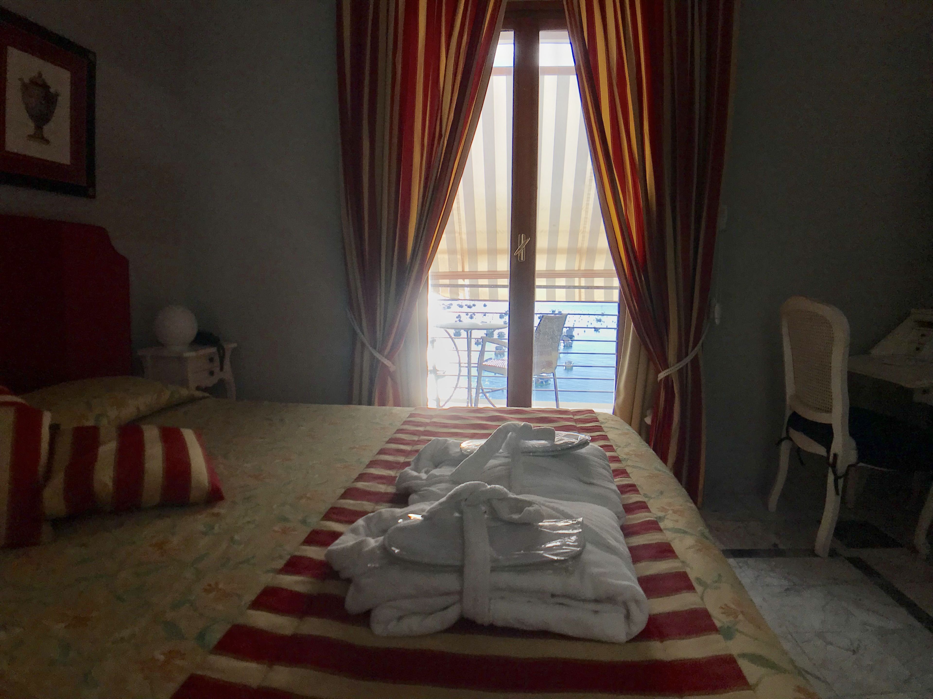 A hotel room with a bed, a chair, and a view of the sea through curtains.
