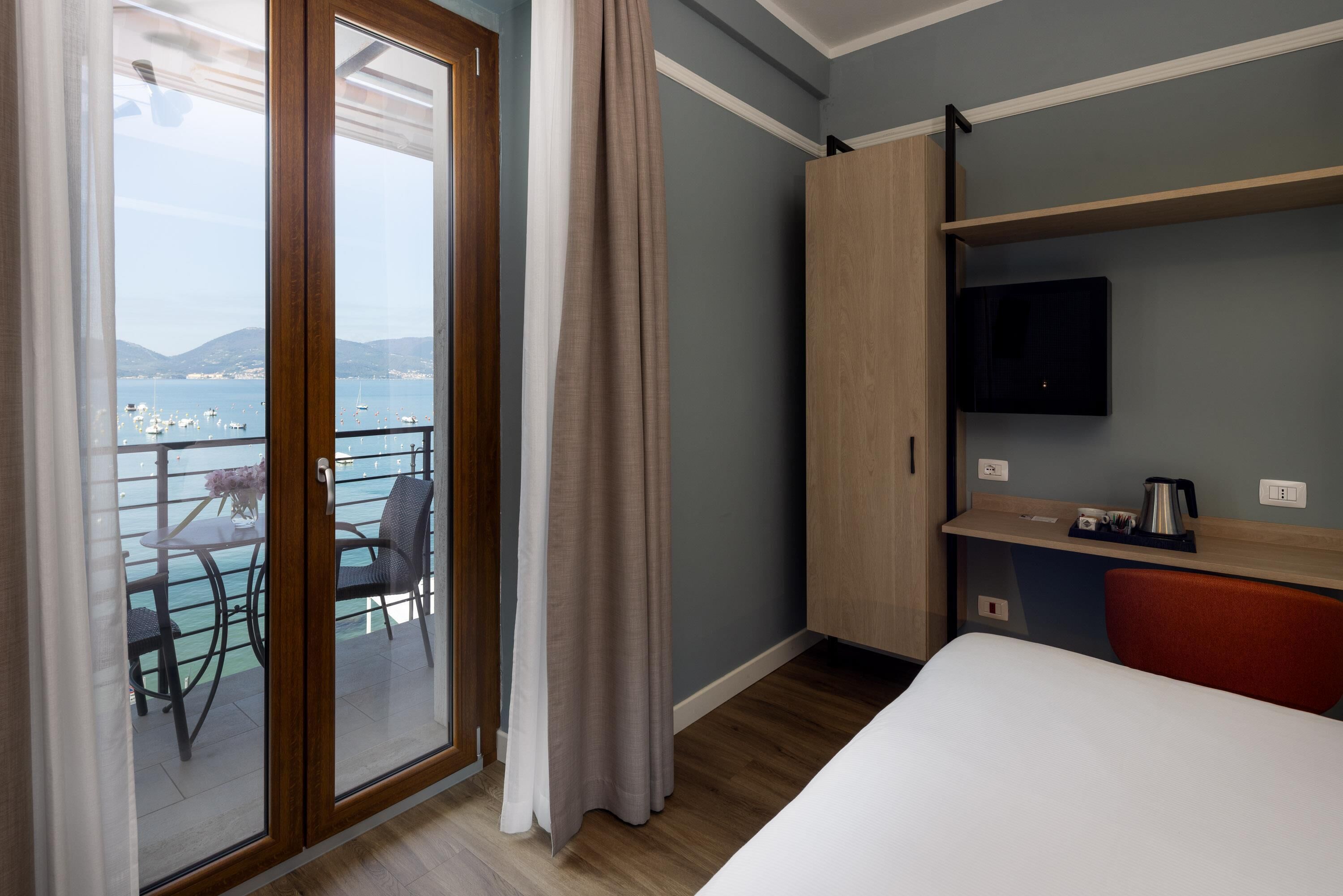 Habitación de hotel con balcón, cama, televisor y escritorio con hervidor.