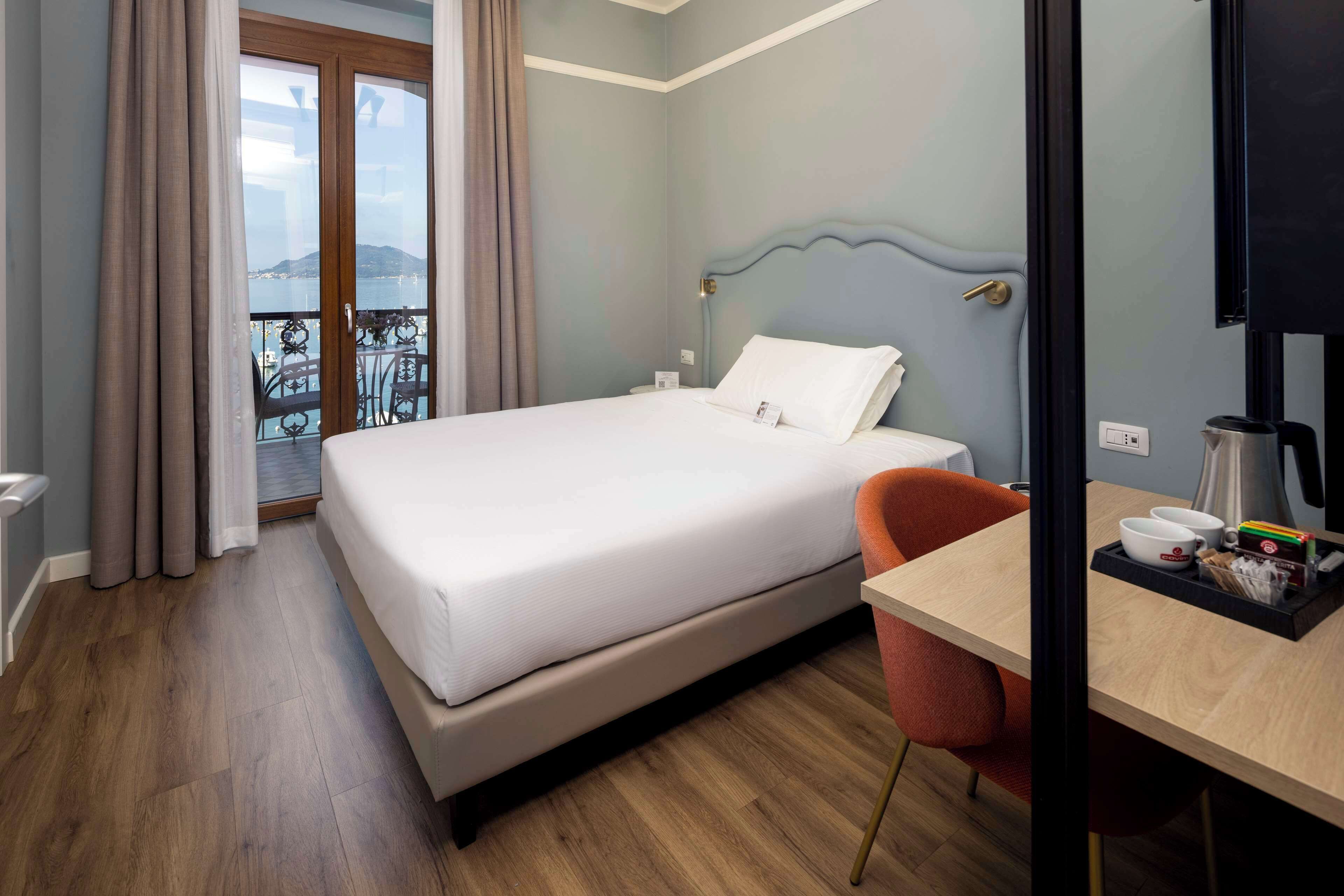Ett hotellrum med en säng, ett skrivbord med en stol, en kaffebryggare och utsikt över havet genom fönstret.