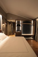 Habitación de hotel con una cama grande, un vestidor, un baño con ducha y bañera, y una mesita con hervidor.