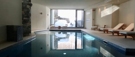 An indoor swimming pool with a stone wall and a view of a rocky landscape.