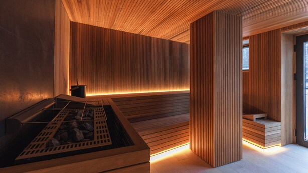 Een moderne sauna met houten lambrisering, vloerverwarming en een zitgedeelte met banken.