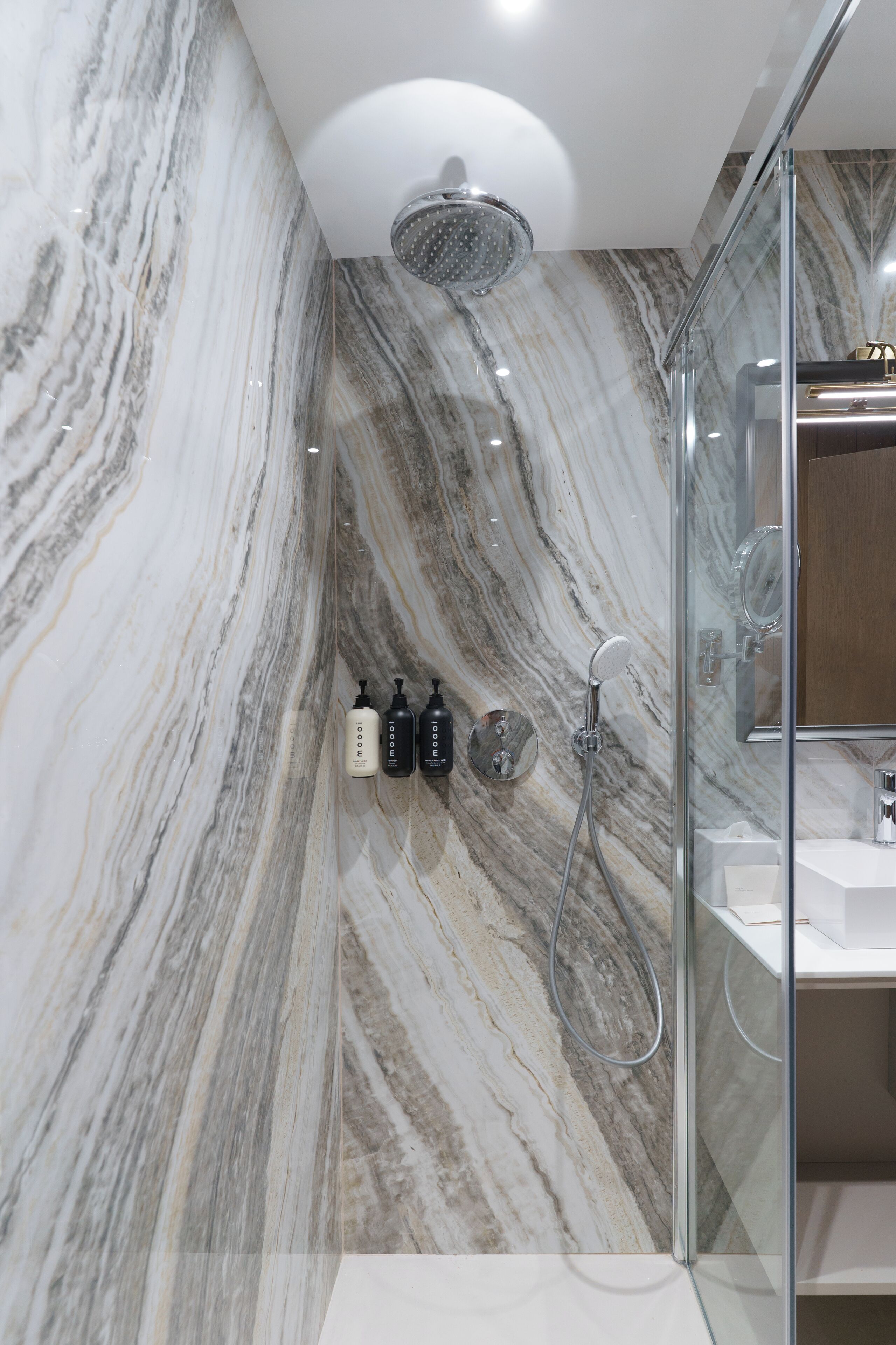 Un baño moderno con pared de mármol, cabina de ducha de vidrio y lavabo blanco.