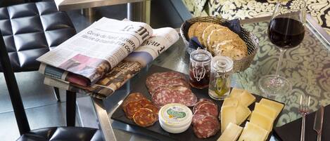 A table with a newspaper, bread, cheese, salami, and a glass of red wine.