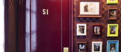 A maroon door with the number 51, a wall with framed photographs, and a checkered pattern.