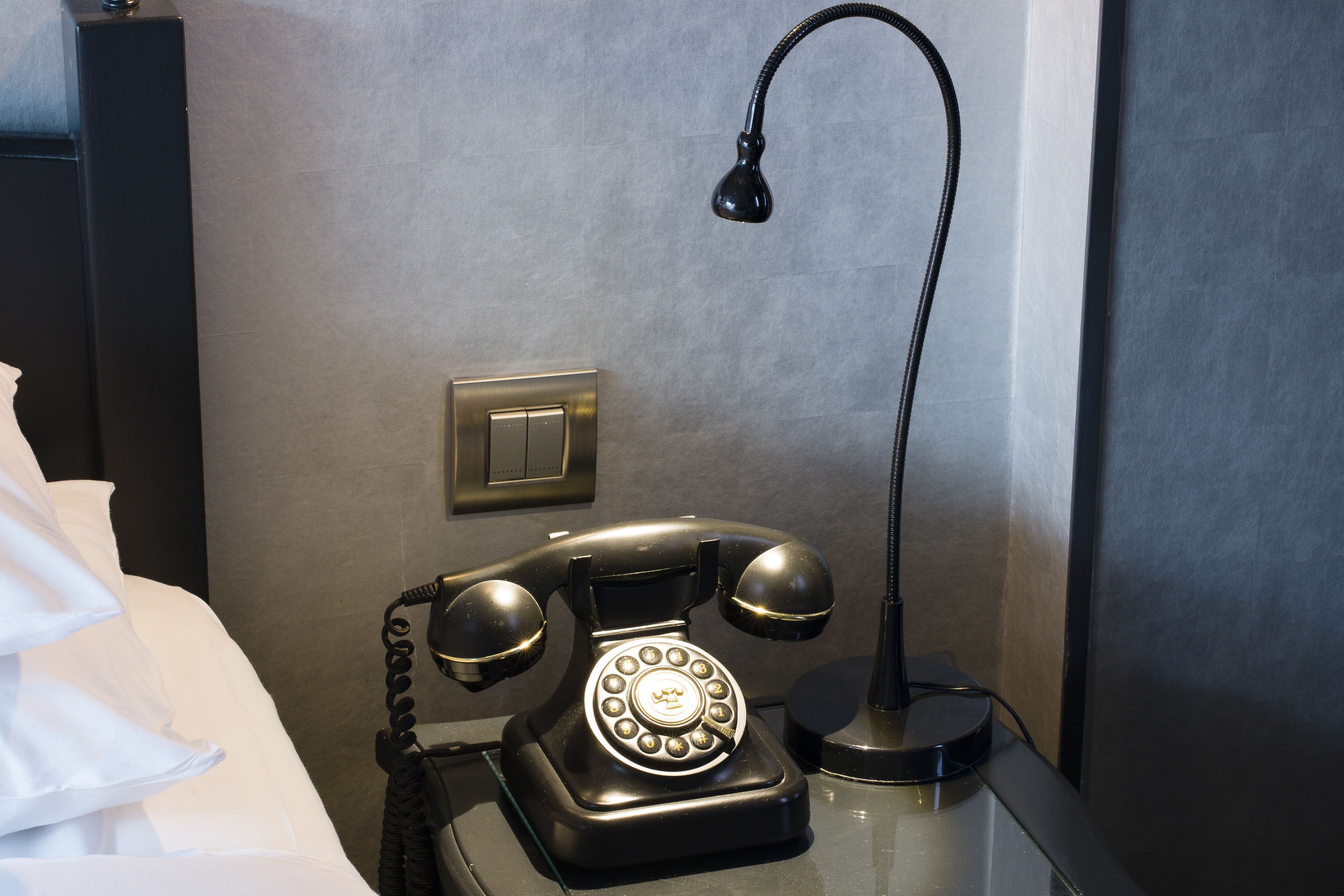 A black rotary phone on a bedside table with a lamp.