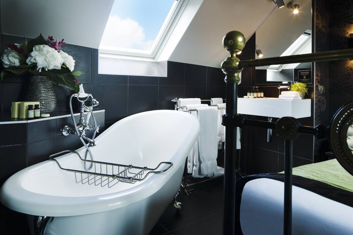 A modern bathroom with a freestanding bathtub, a vanity with a mirror, and a skylight above the sink.