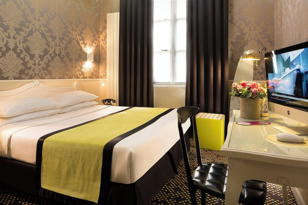 A hotel room with a bed, a desk with a computer, a chair, a lamp, and a TV.