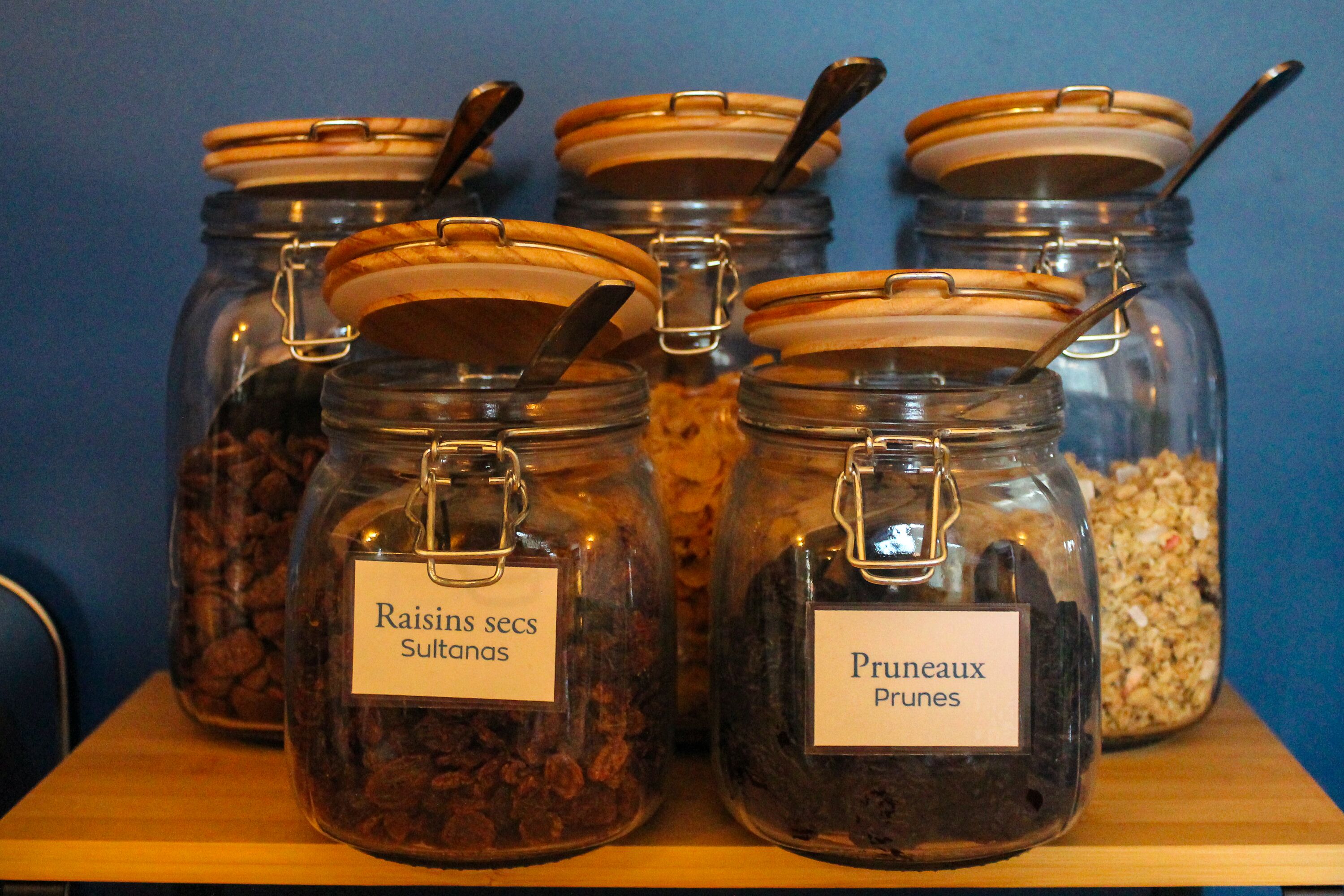 Glass jars with metal lids and labels on a wooden shelf against a blue wall.