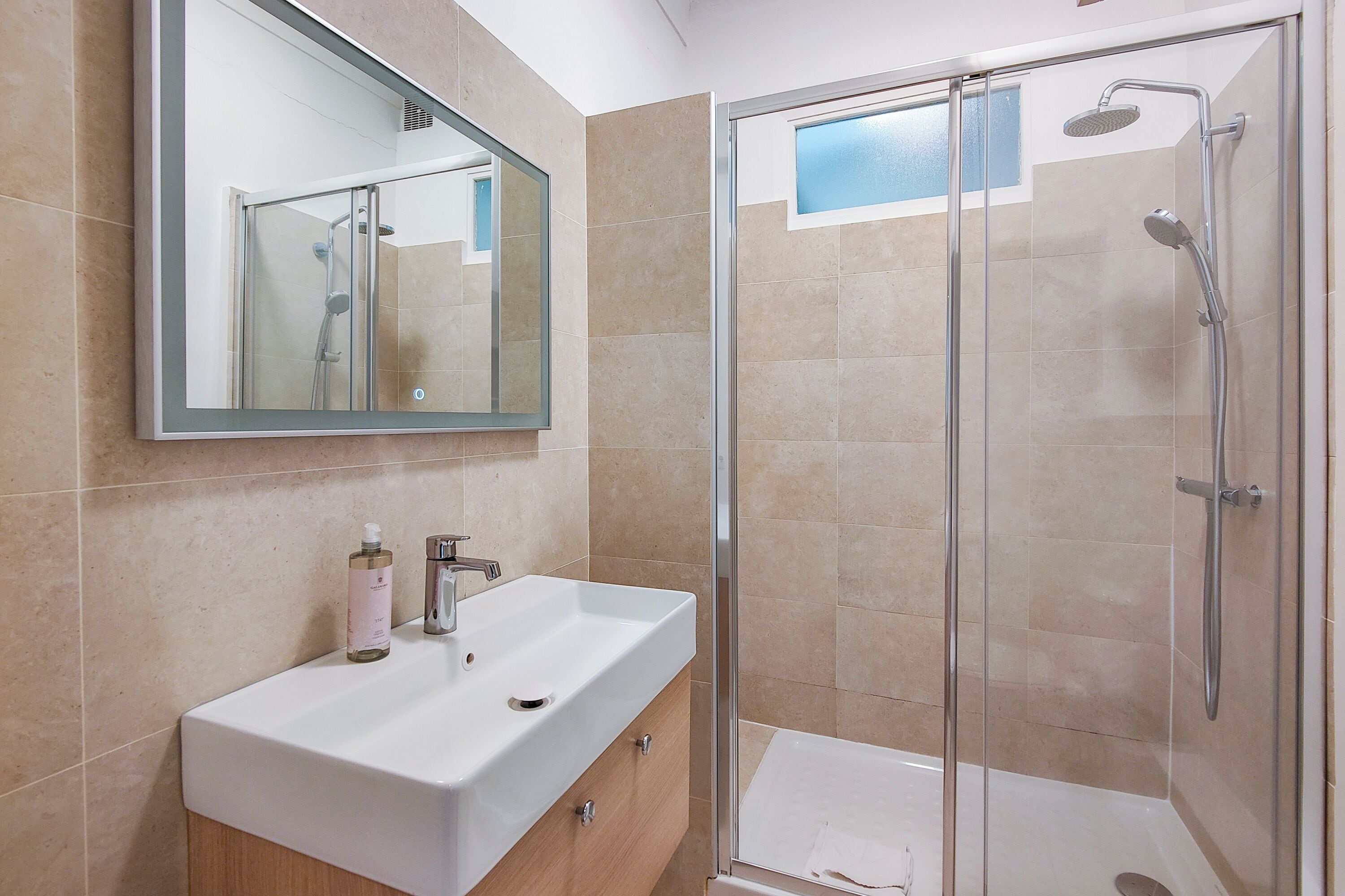 A modern bathroom with a glass-enclosed shower, a white sink, and a mirror above it.