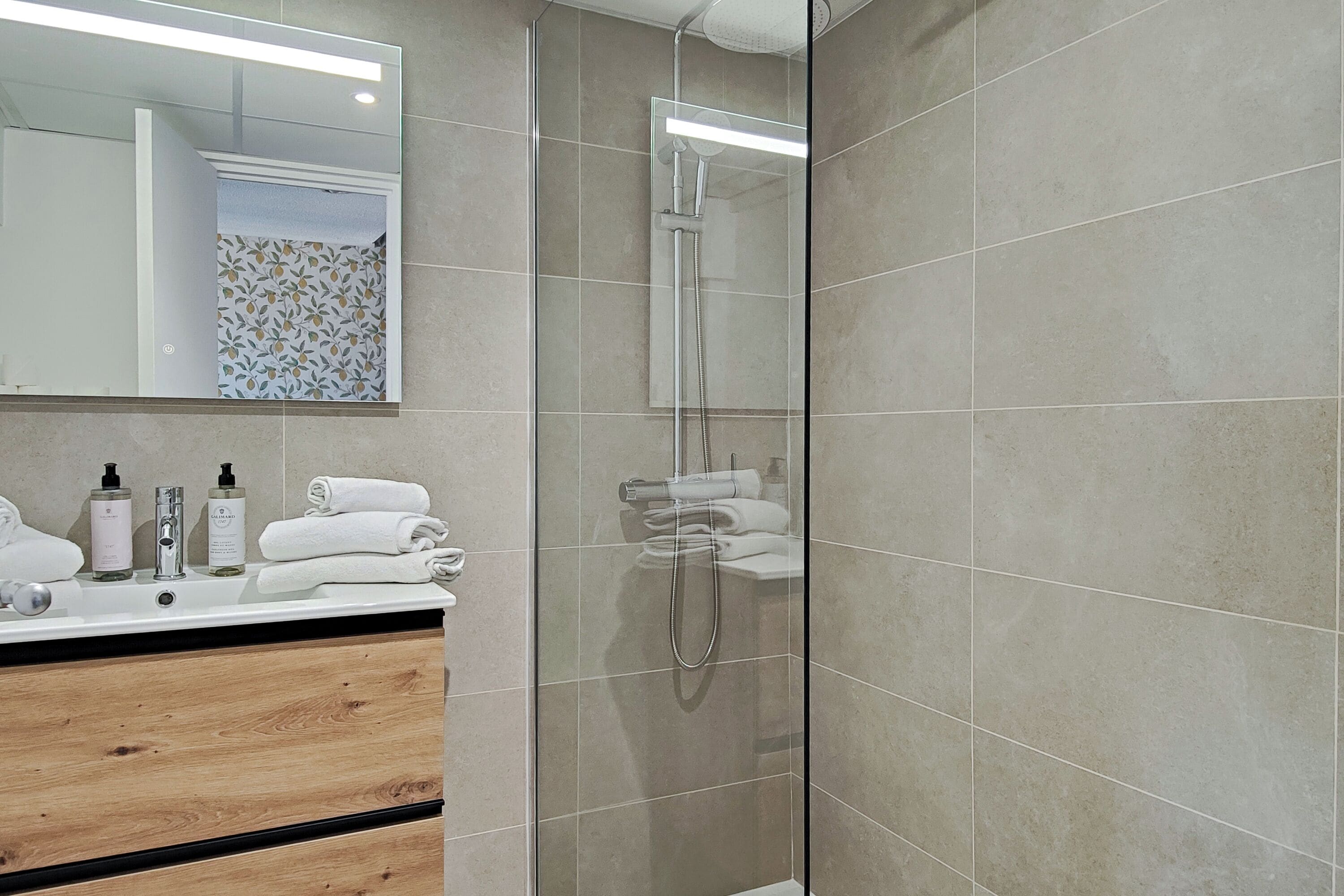 A modern bathroom with a glass-enclosed shower, a wooden vanity, and a mirror above the sink.