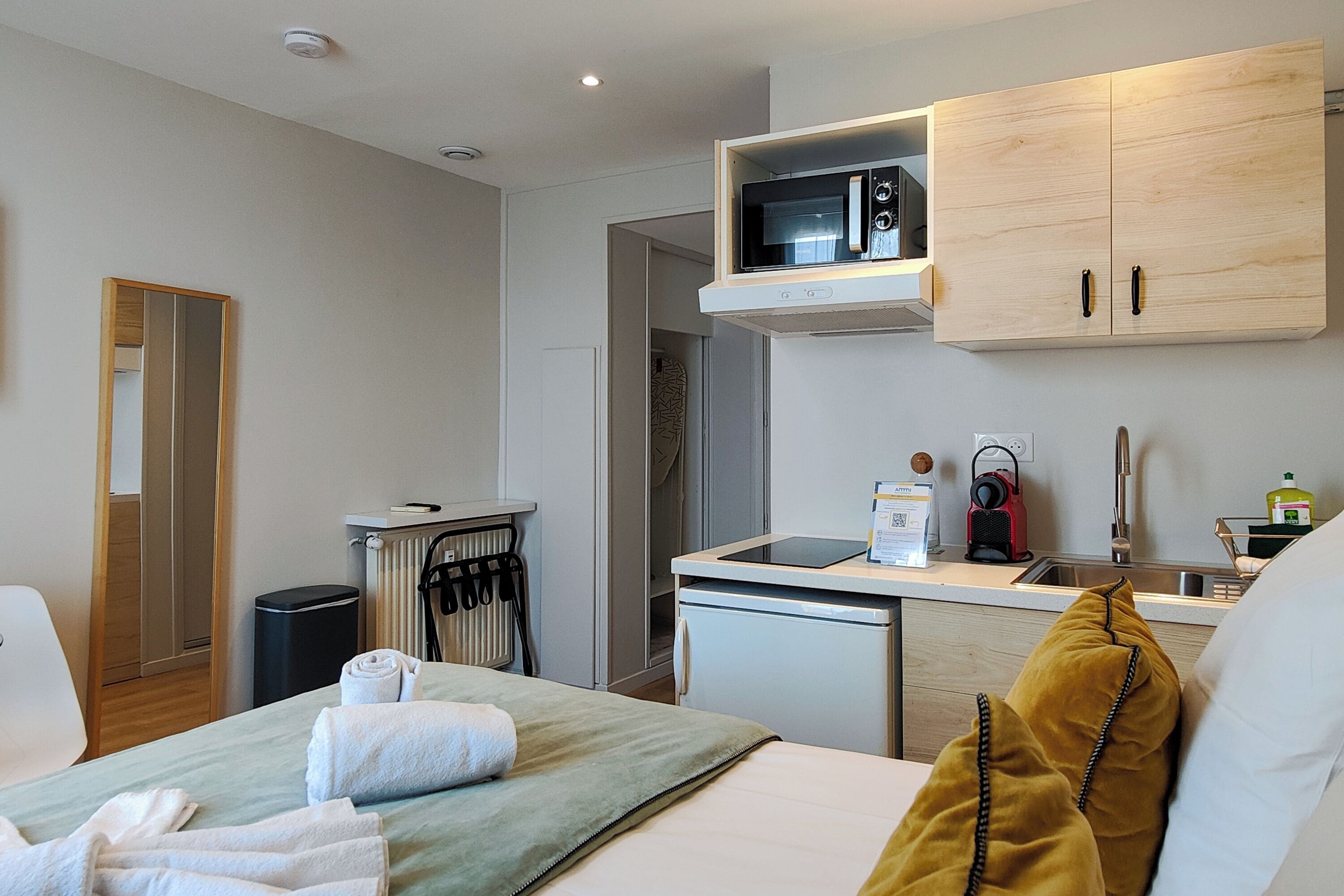 Una habitación de hotel moderna con cama, una kitchenette pequeña, microondas y lavamanos.