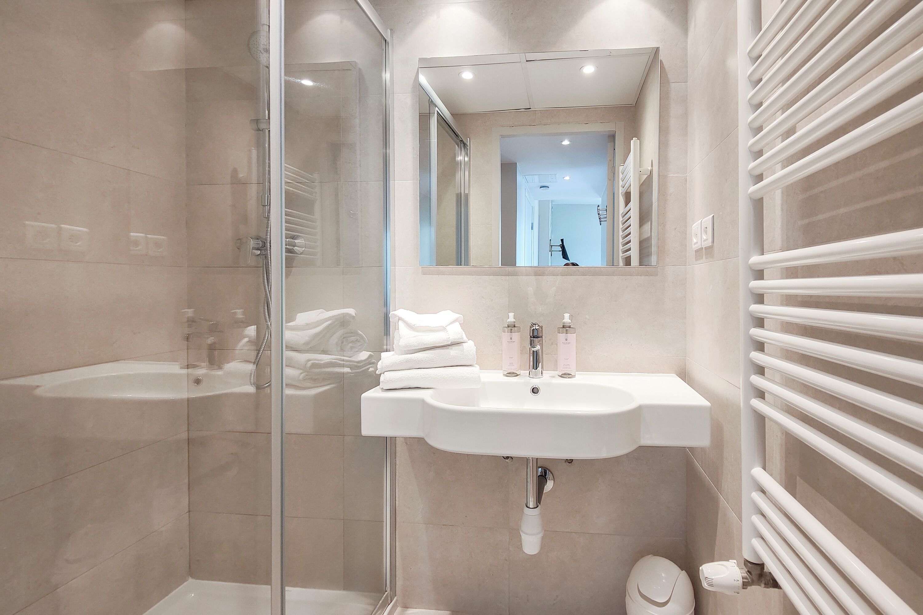 Un baño moderno con cabina de ducha de vidrio, un lavabo blanco con espejo y un perchero para toallas.