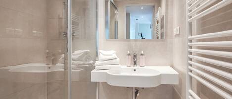 Un baño moderno con cabina de ducha de vidrio, un lavabo blanco con espejo y un perchero para toallas.