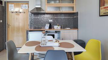 A compact kitchen with a microwave, a small refrigerator, and a sink. There are two chairs and a table with a tray.