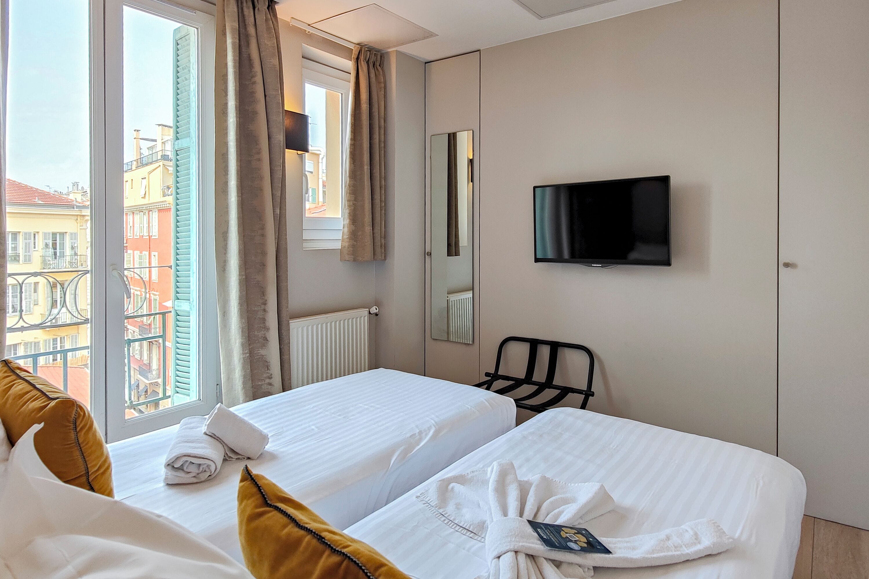 A hotel room with two beds, a TV, a mirror, and a window with curtains.