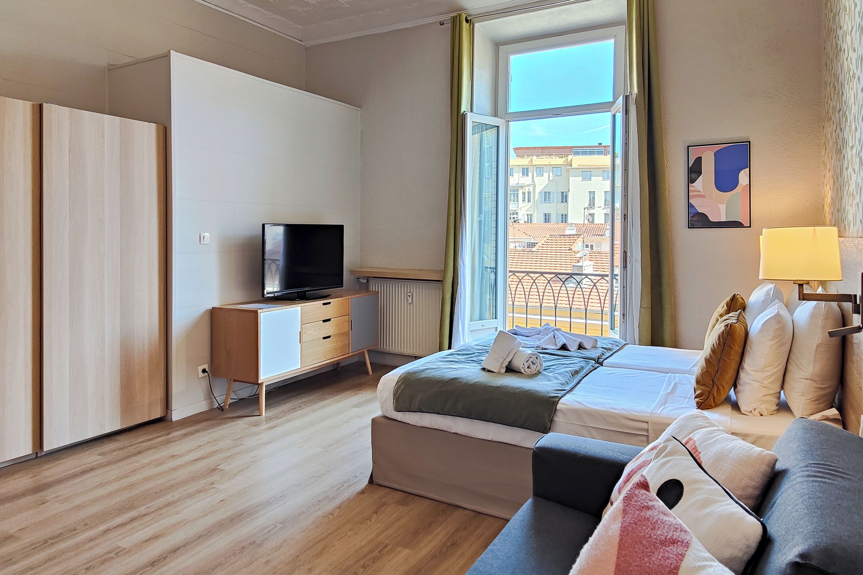 Ein modernes Hotelzimmer mit Bett, Fernseher, Sofa und einem Fenster mit Blick auf Gebäude.