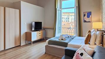 A modern hotel room with a bed, a TV, a sofa, and a window with a view of buildings.